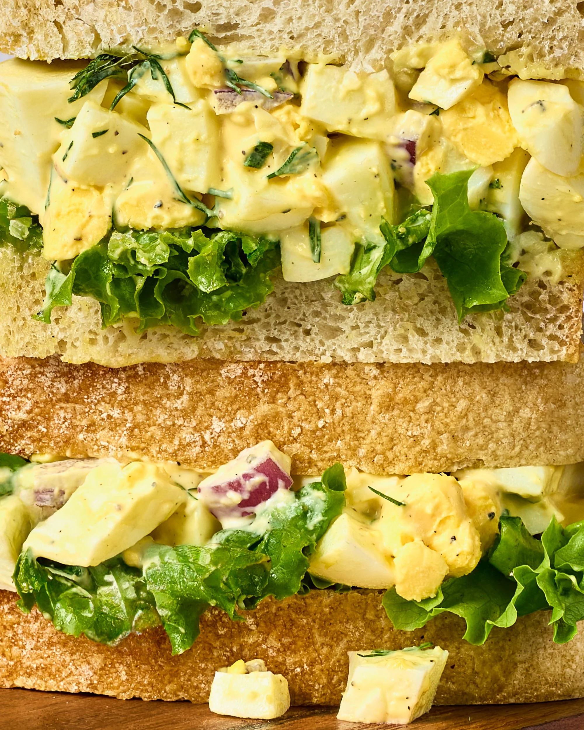 Close-up of two sandwiches with egg salad, lettuce, and bread, stacked on top of each other.