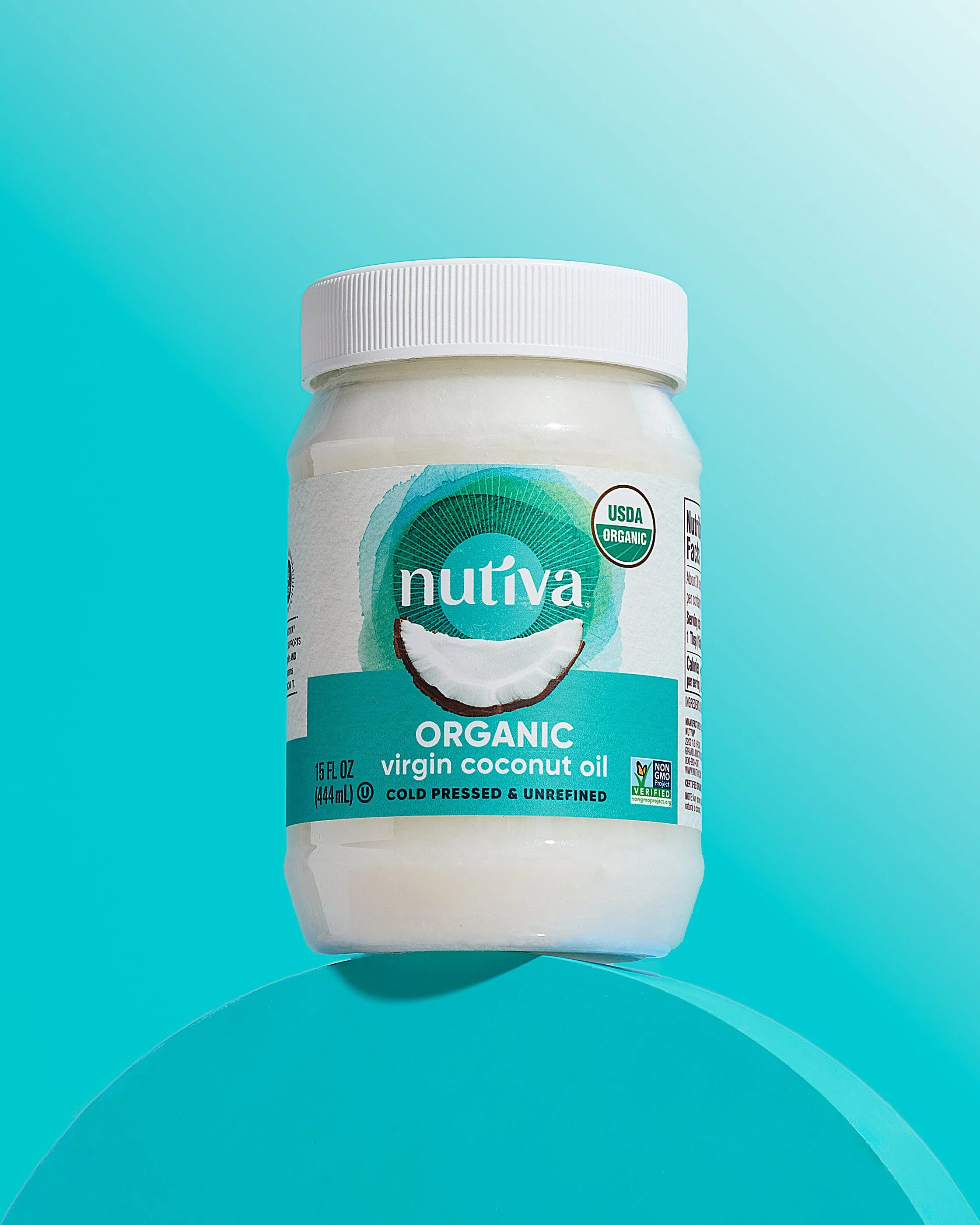 Container of Nutiva organic virgin coconut oil on a curved reflective surface with a light blue background.