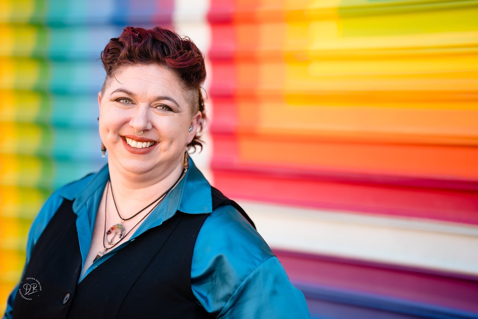 Mara smiling in front of a rainbow mural