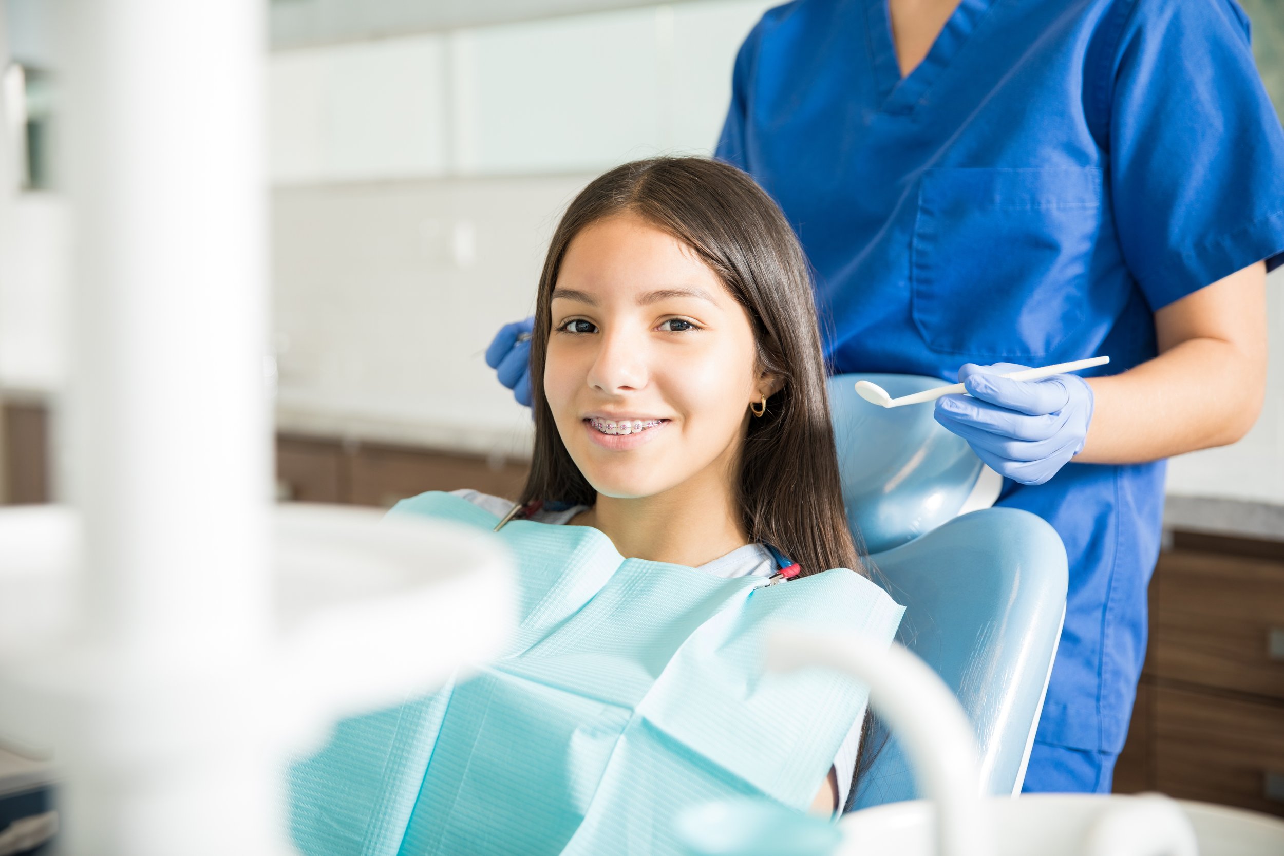 portrait-smiling-teenage-girl-with-braces-sitting-chair-while-dentist-standing-clinic.jpg