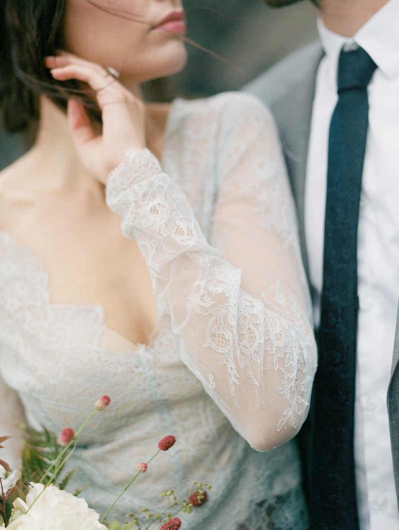 Bride in lace wedding dress with bouquet standing next to groom in suit and tie.