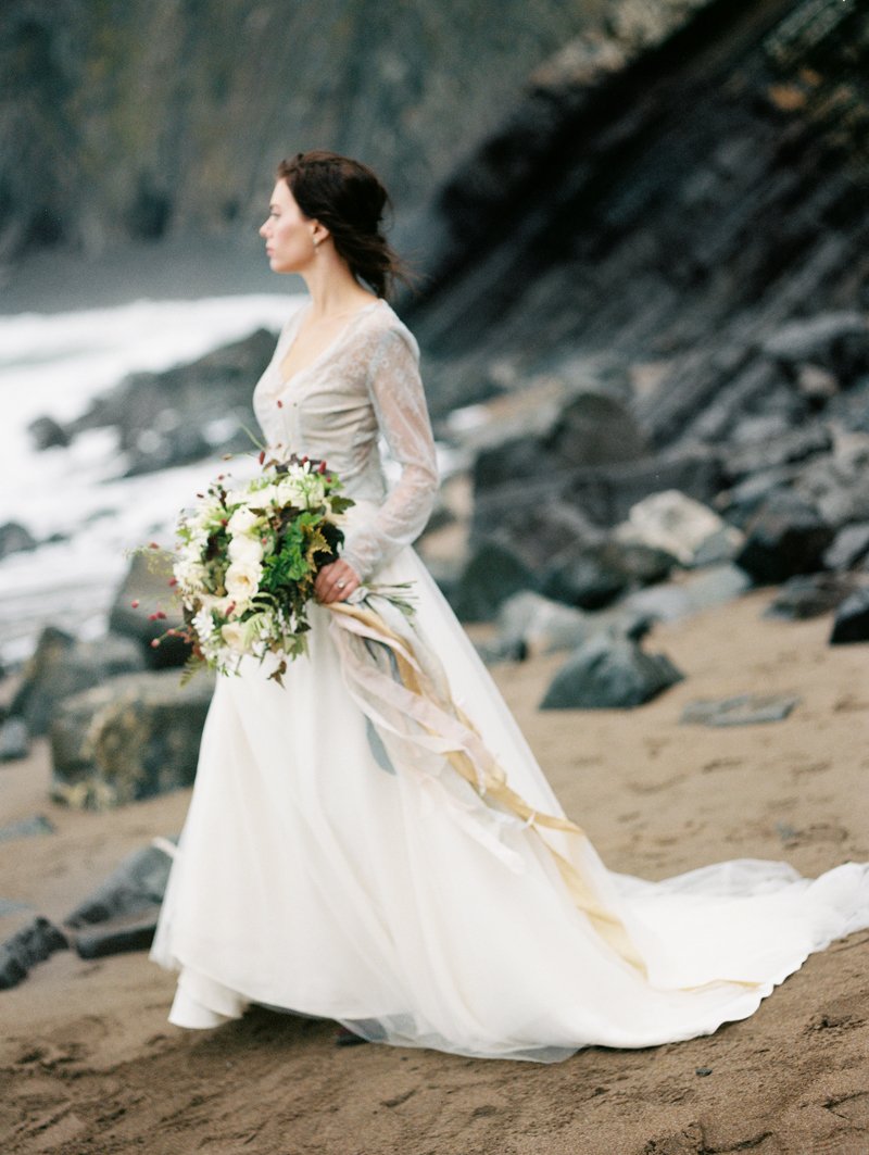 Bride in white dress holding bouquet on rocky beach