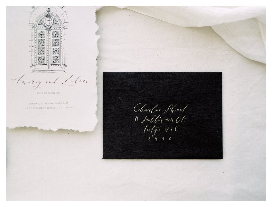 Wedding invitation and black envelope with handwritten address on white background.