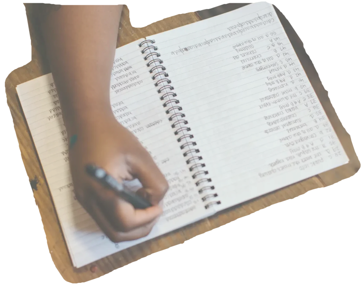 A person writing in a spiral notebook on a wooden table.