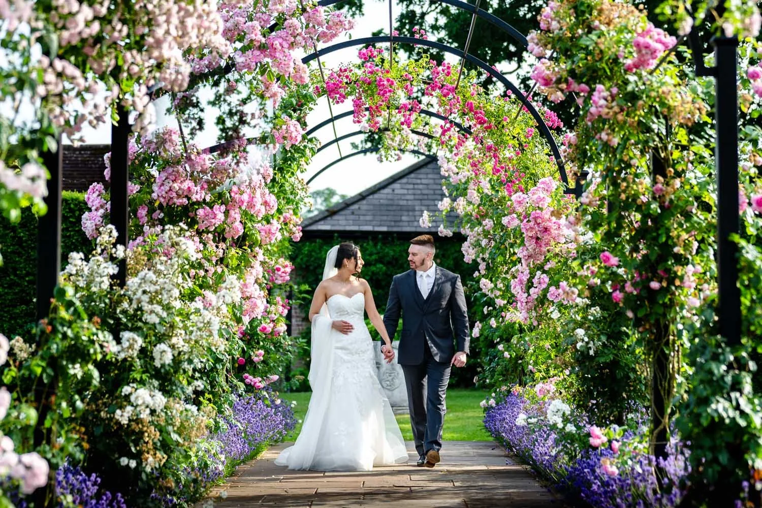 A bride and groom walk through a stunning flower display at Micklefield Hall in Rickmansworth. Photography by Steve Bagness
