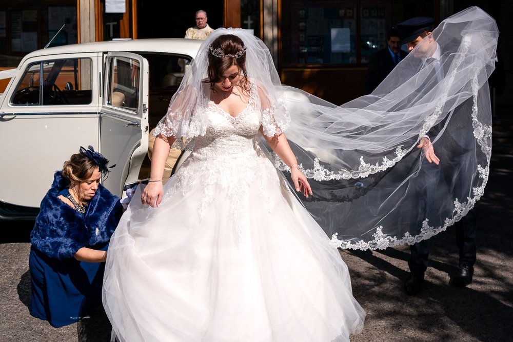 Bride has her wedding veil fanned out after arriving at church