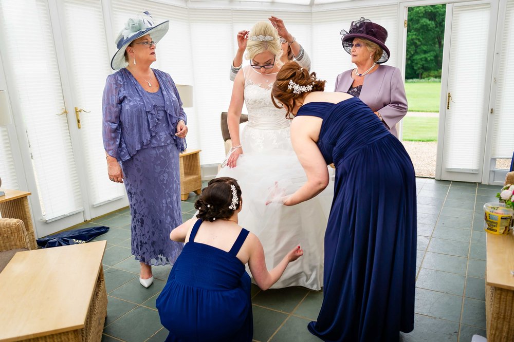 Bridal party fuss over a brides dress as she gets ready at Warbrook House