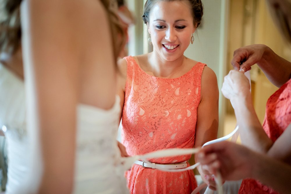 Bridesmaid tying bride into dress, Donnington Valley Hotel, Newbury