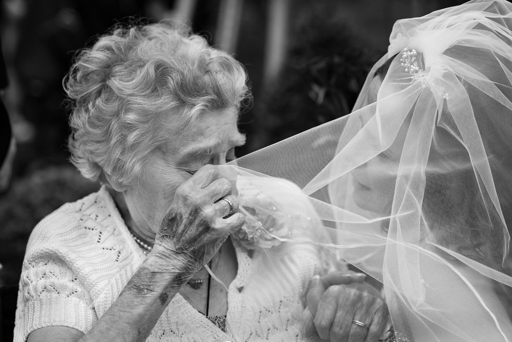 Grandmother wipes away a tear using the brides veil