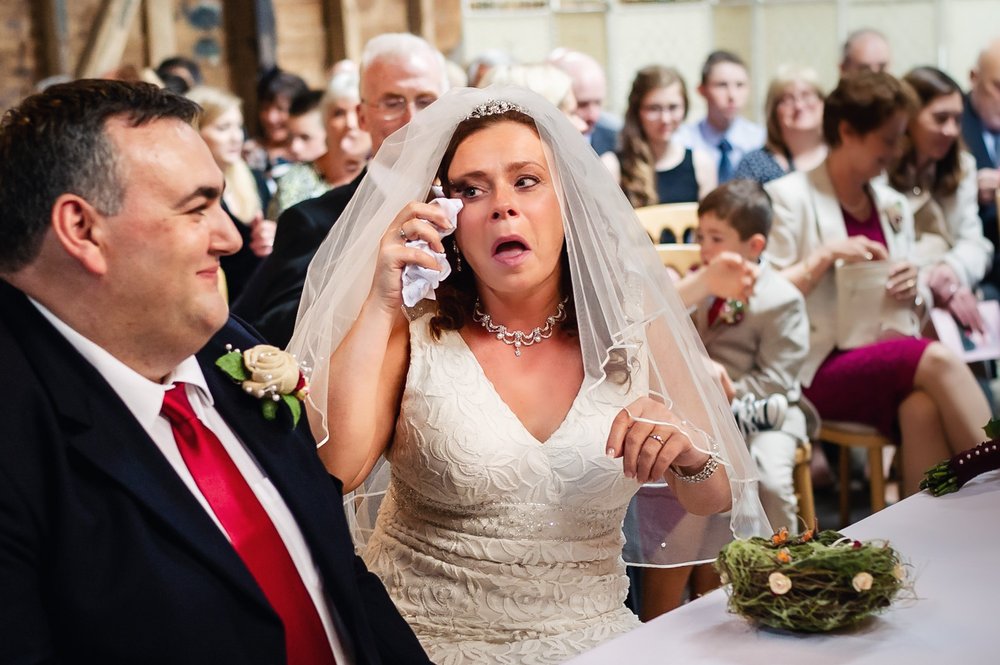 Brides dabs a tear from her eye during wedding ceremony