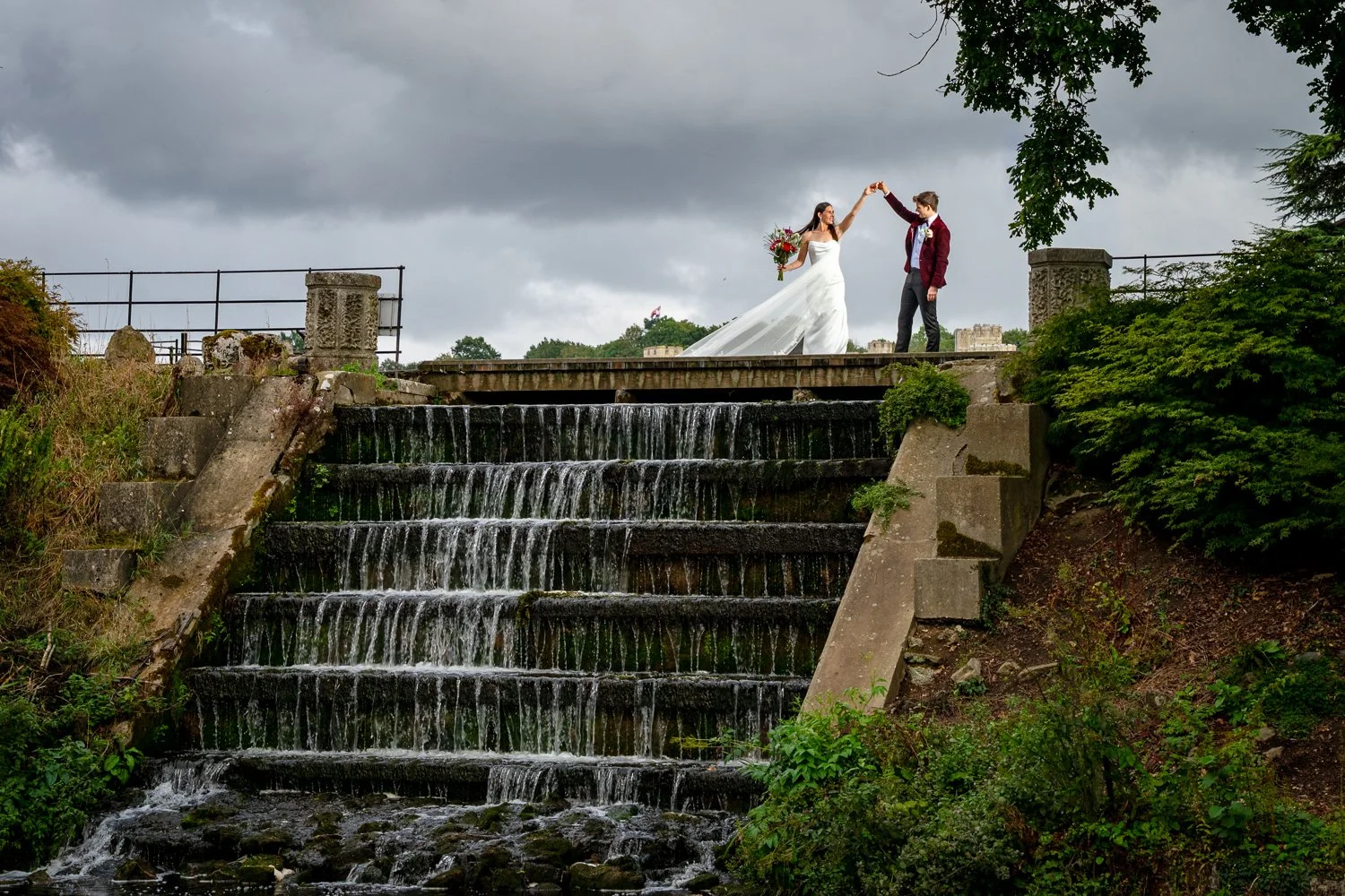 A bride and groom practice their first dance on top of a waterfall at Leeds Castle in Kent. Photographed by Steve Bagness, 
documentary wedding photographer.