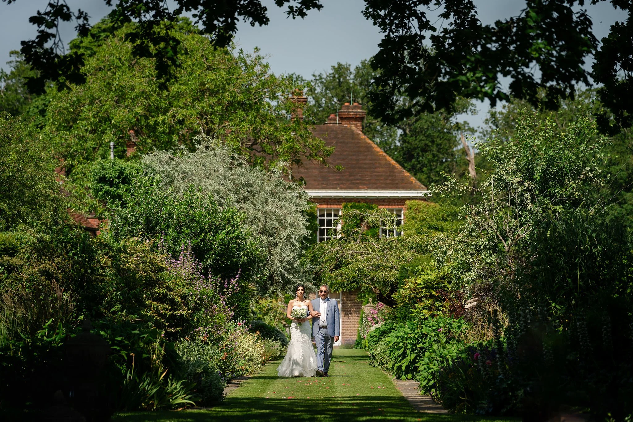 A father of the bride walks his daughter to the outdoor ceremony at Micklefield Hall in Rickmansworth
