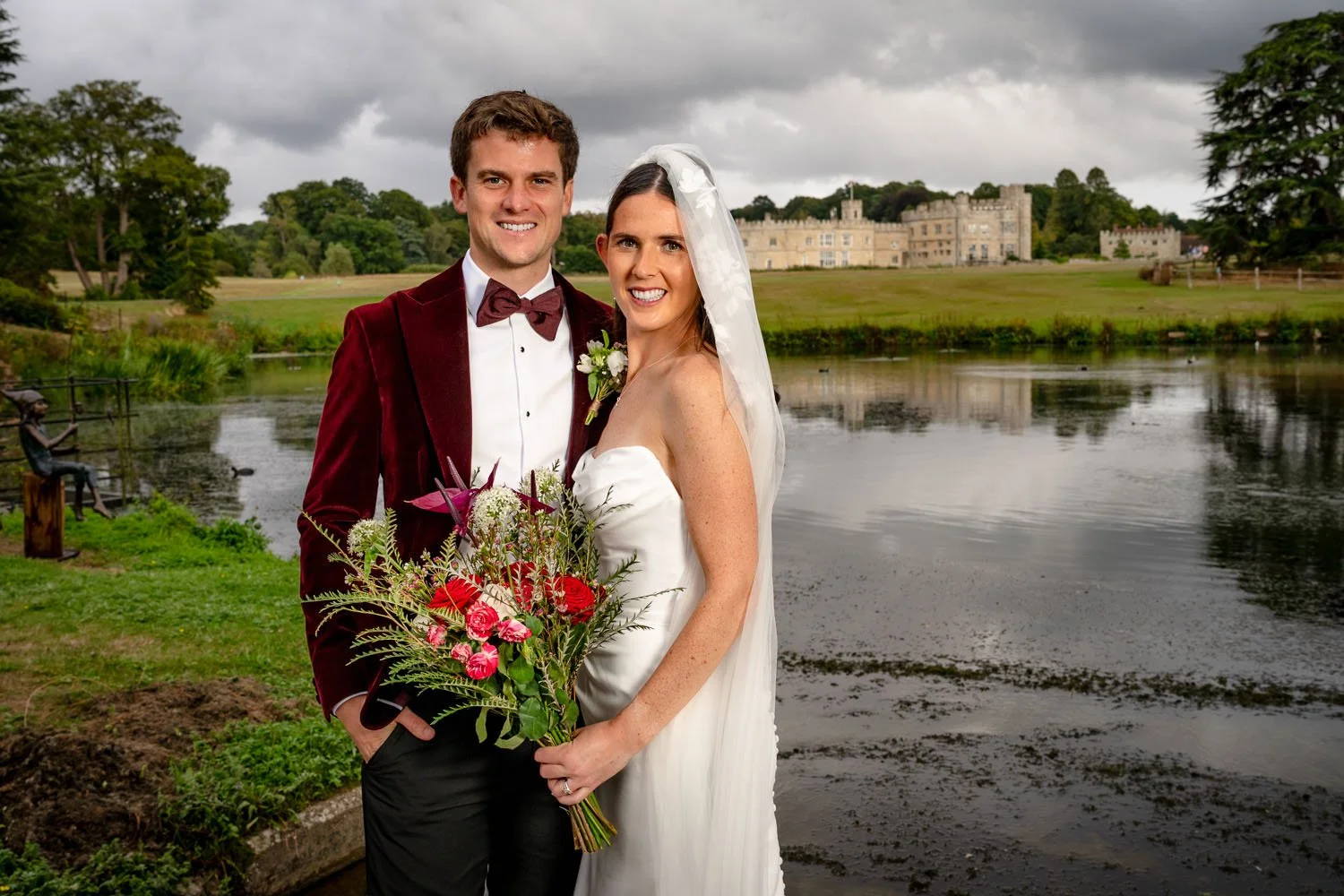 A bride and groom pose for a portrait with Leeds Castle in the background. Photographed by Steve Bagness, documentary wedding photographer.
