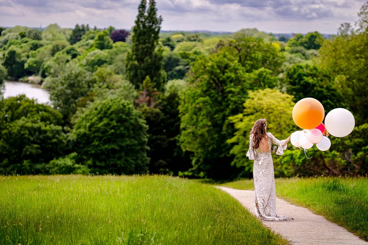 A bride in a shimmering backless gold dress holds balloons aloft on Richmond Hill. Photograph by Steve Bagness