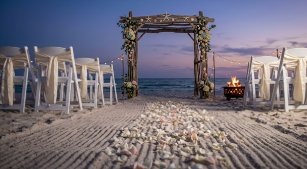Beach wedding reception with raked sand aisle, sashed chairs, starfish arbor, and bonfire setup in Panama City Beach.