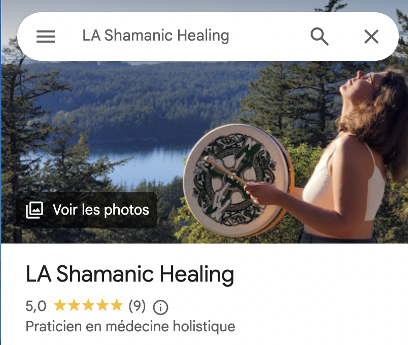 A woman outdoors holding a drum, with a lake and trees in the background, during daytime.