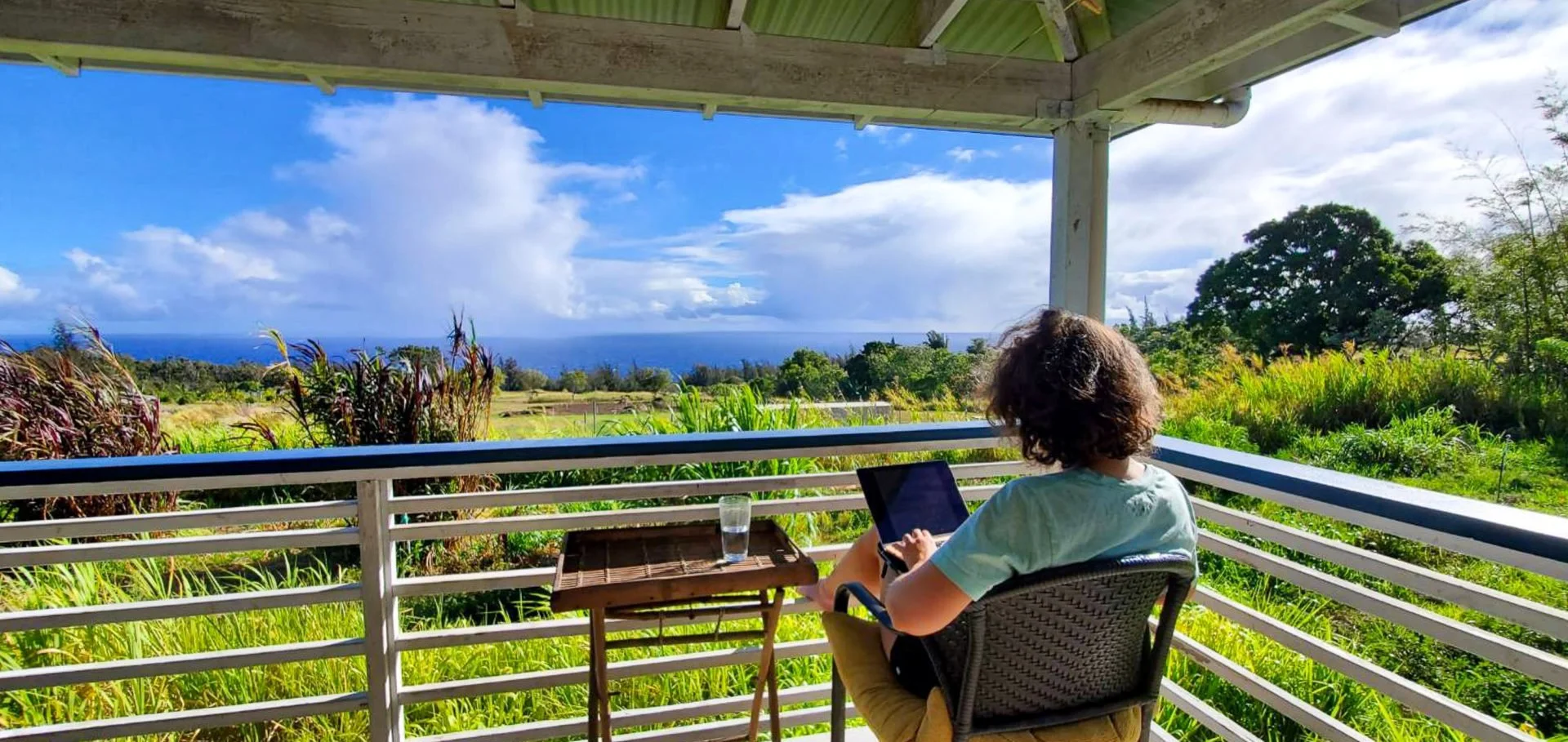 A writer on a wooden terrace writes facing the pacic ocean and green fields
