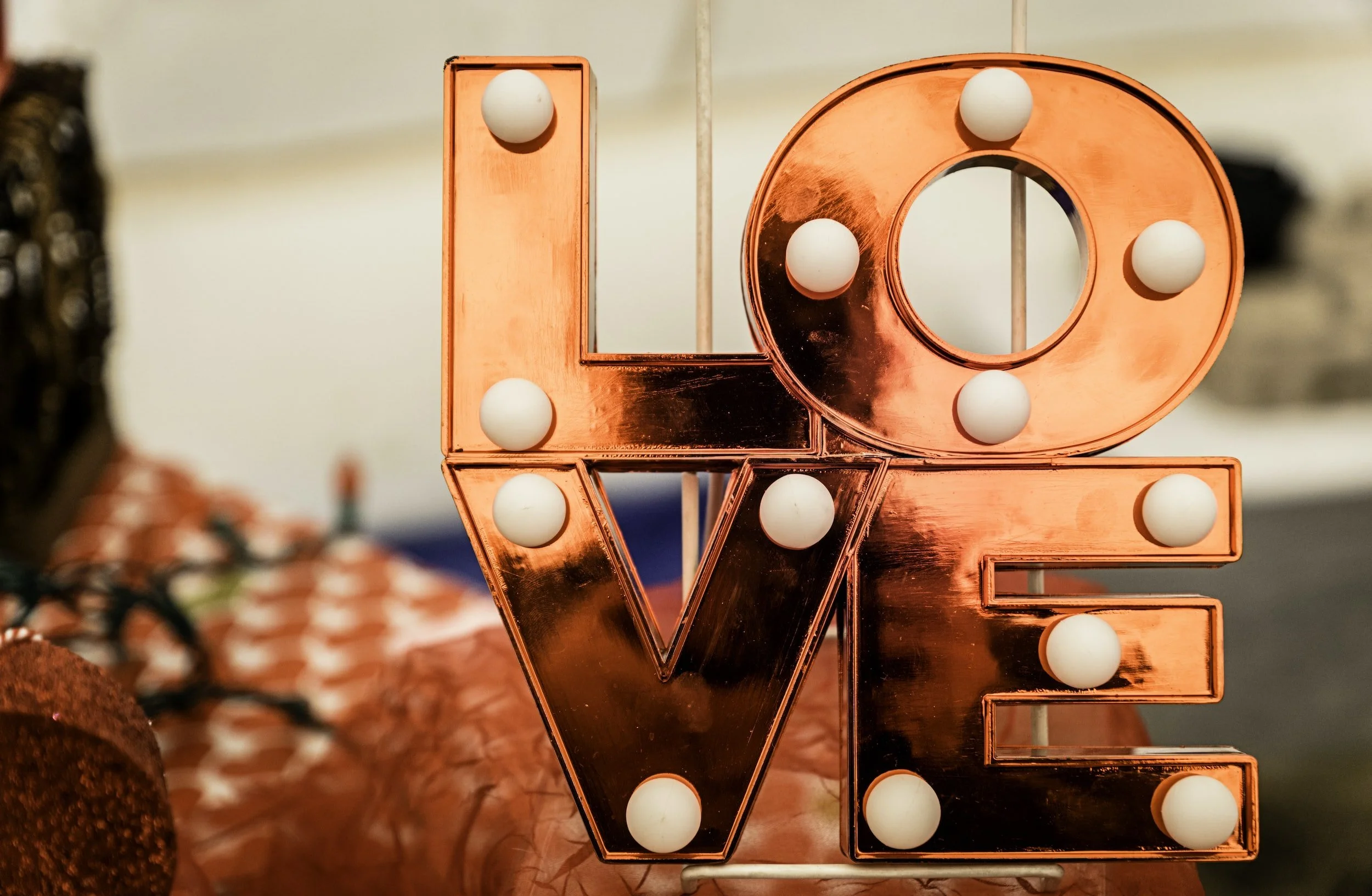 Decorative love sign with illuminated round light bulbs, featuring the letters L, O, V, and E in a metallic rose gold finish.