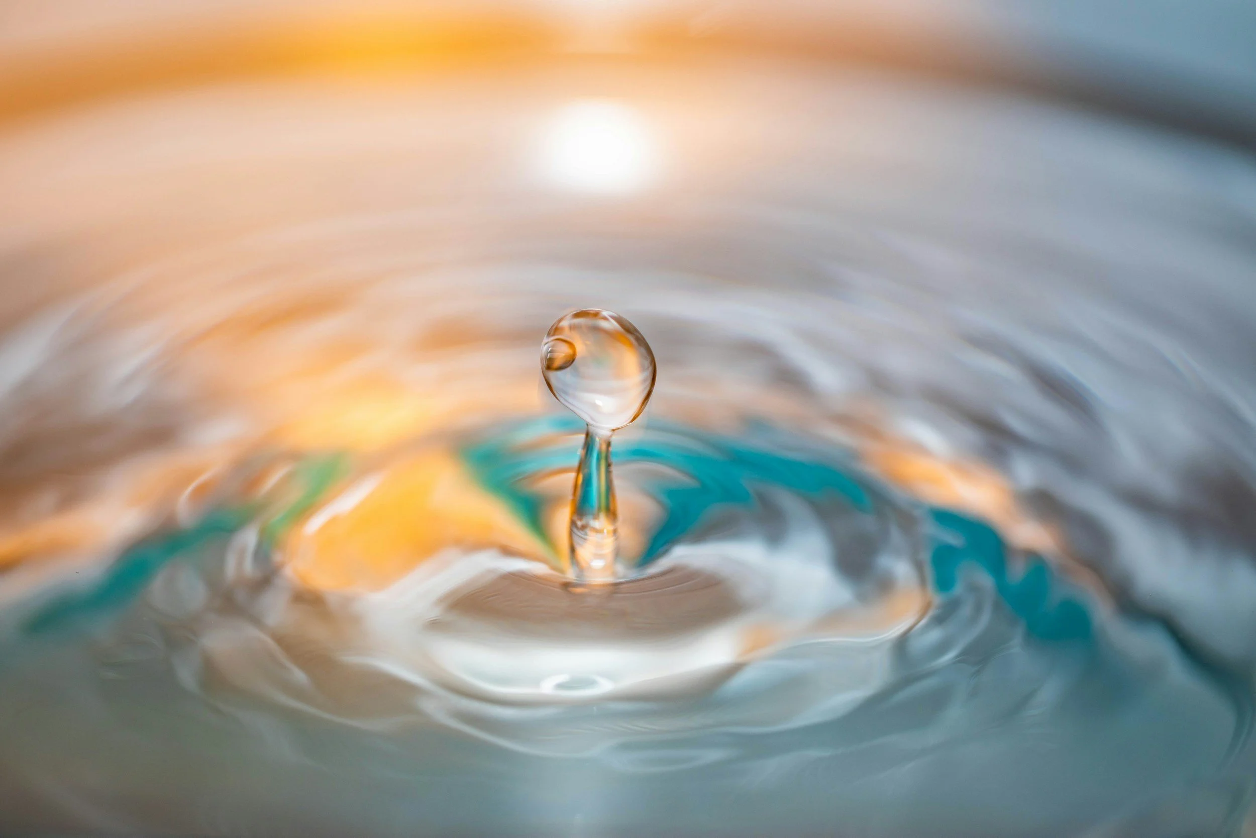 Close-up of a water droplet splashing into a calm body of water, creating ripples and a bubble at the center.