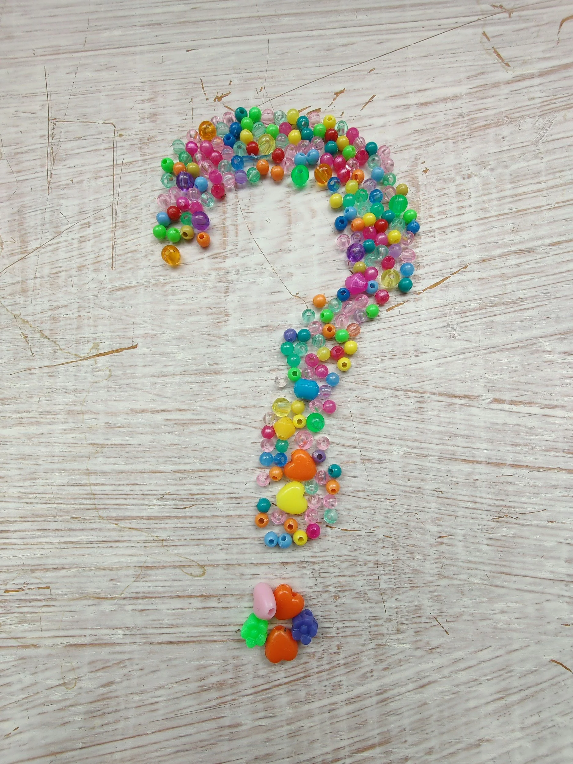 Colorful plastic beads arranged in the shape of a question mark on a wooden surface.