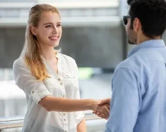A woman smiling and shaking hands with a man indoors.