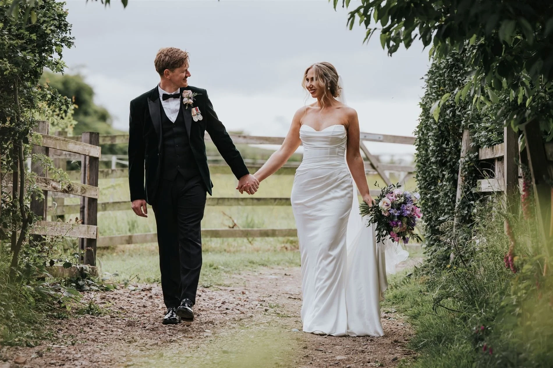 bride and groom walking down dirt track holding hands