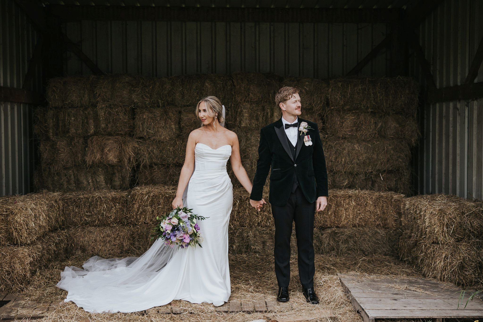 bride and groom in hay bale barn holding hands
