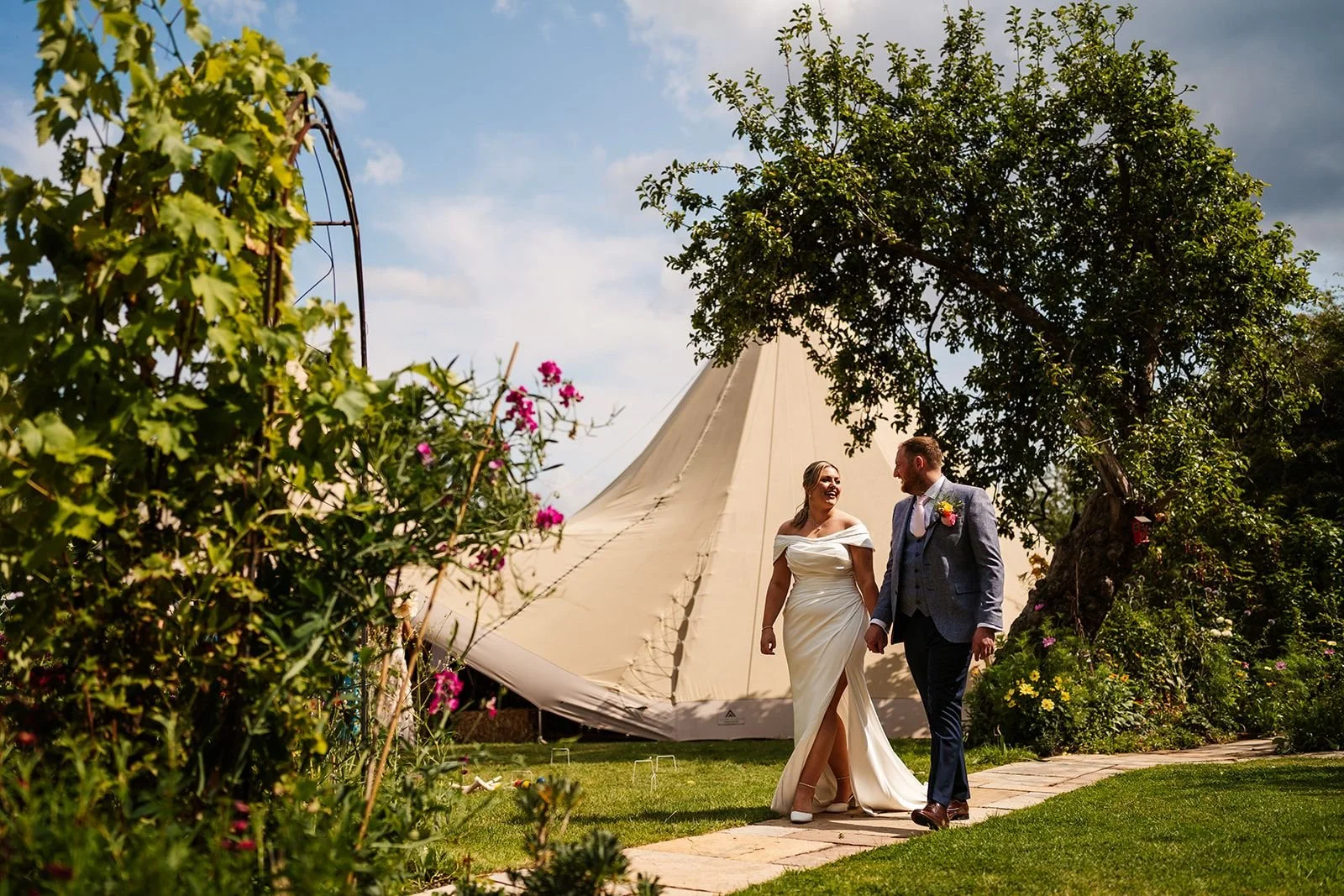 bride and groom walking with wedding tipi behind them