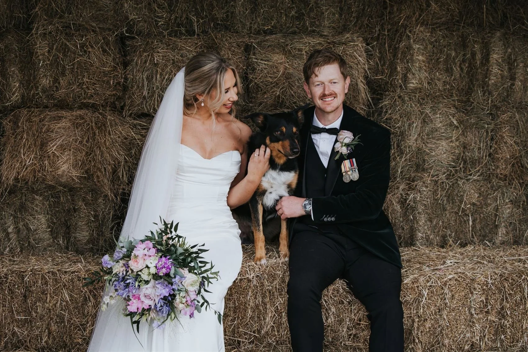 bride and groom on haybales with their dog
