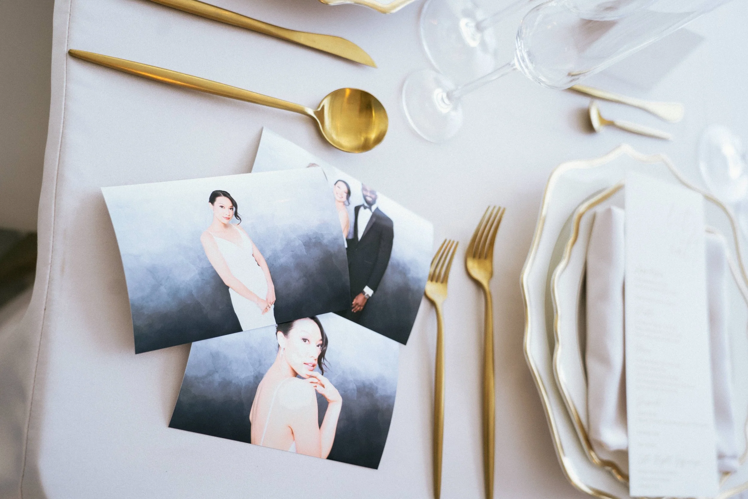 A wedding table setting with gold utensils, glassware, and wedding photos of a woman in a white dress and a man in a tuxedo.