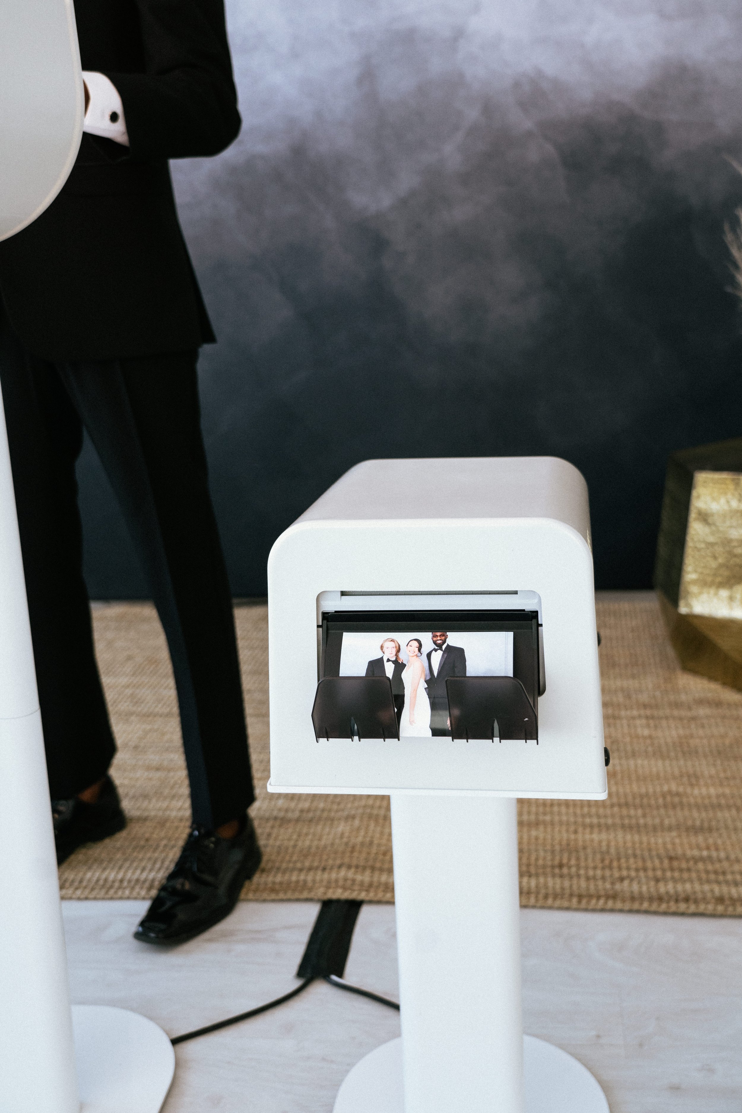 Photo booth prints of a group of three people, including a wedding bride in a gown, at a wedding or event, inside a modern venue.