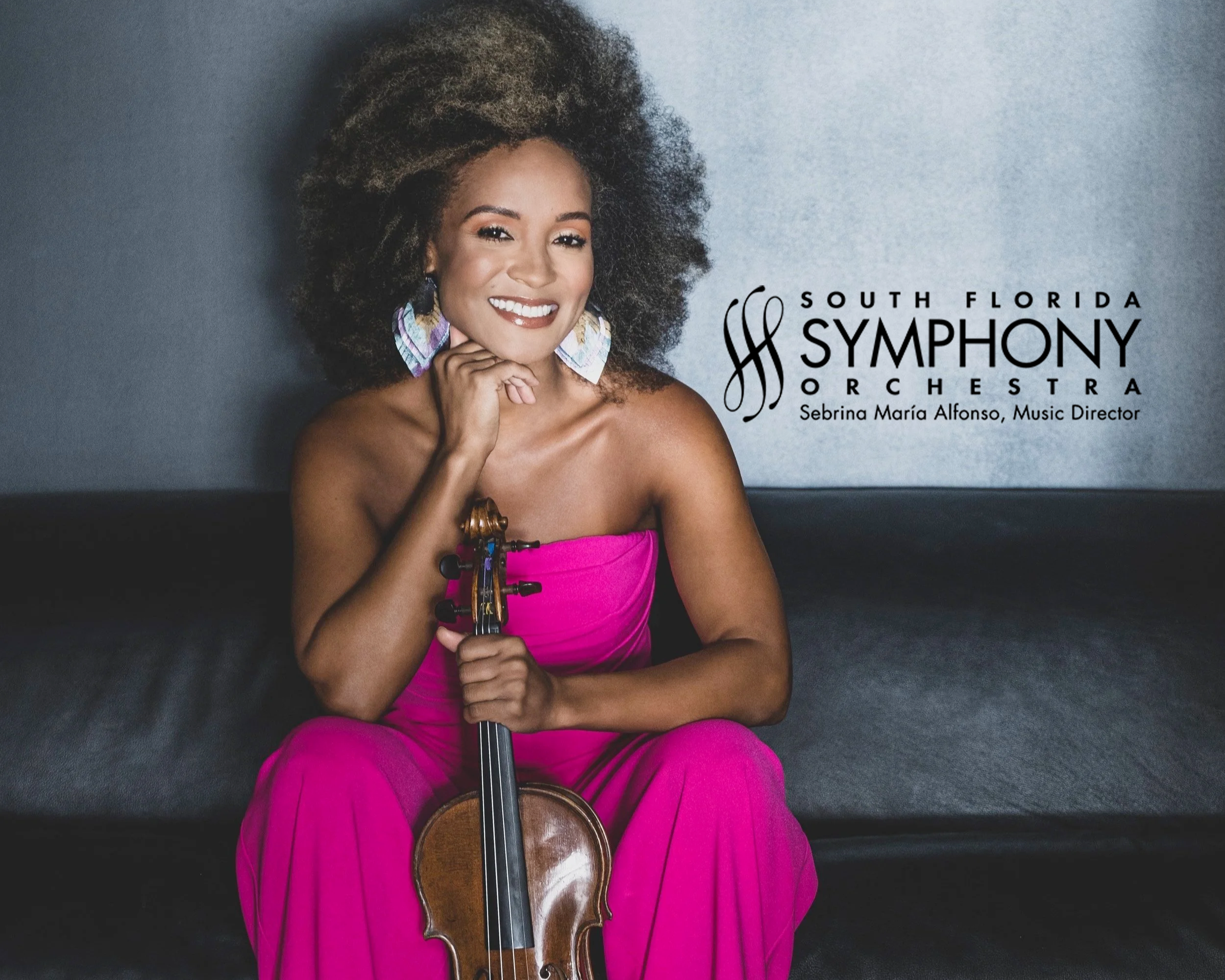 A woman with curly hair wearing a bright pink dress and colorful earrings, holding a violin and bow, smiling at the camera. The background is a simple gray wall, and there is text overlay promoting the South Florida Symphony Orchestra with Sebrina Maria Alfonso as music director.