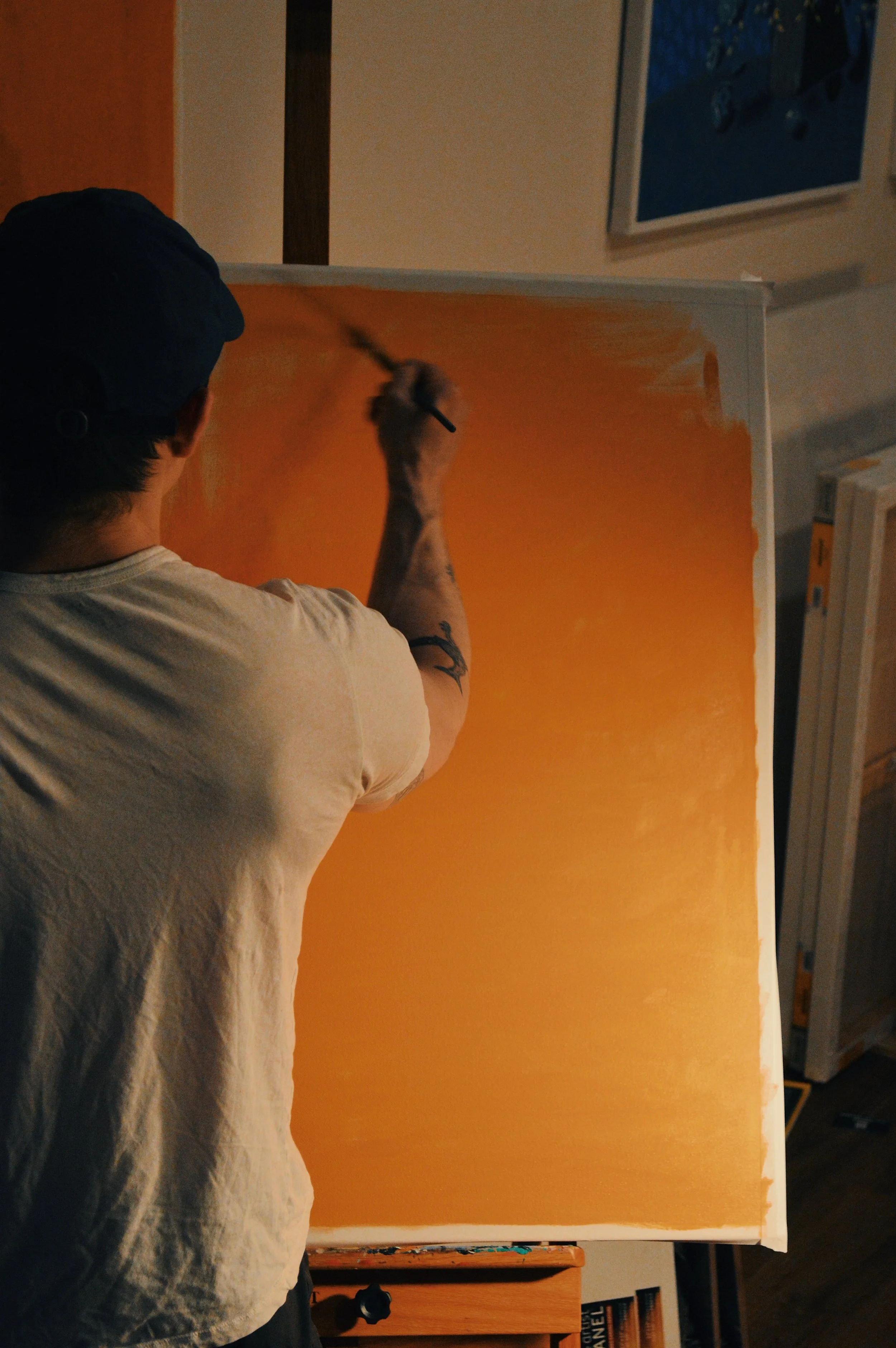 Photograph of Kevin Koza from behind painting an orange underpainting.