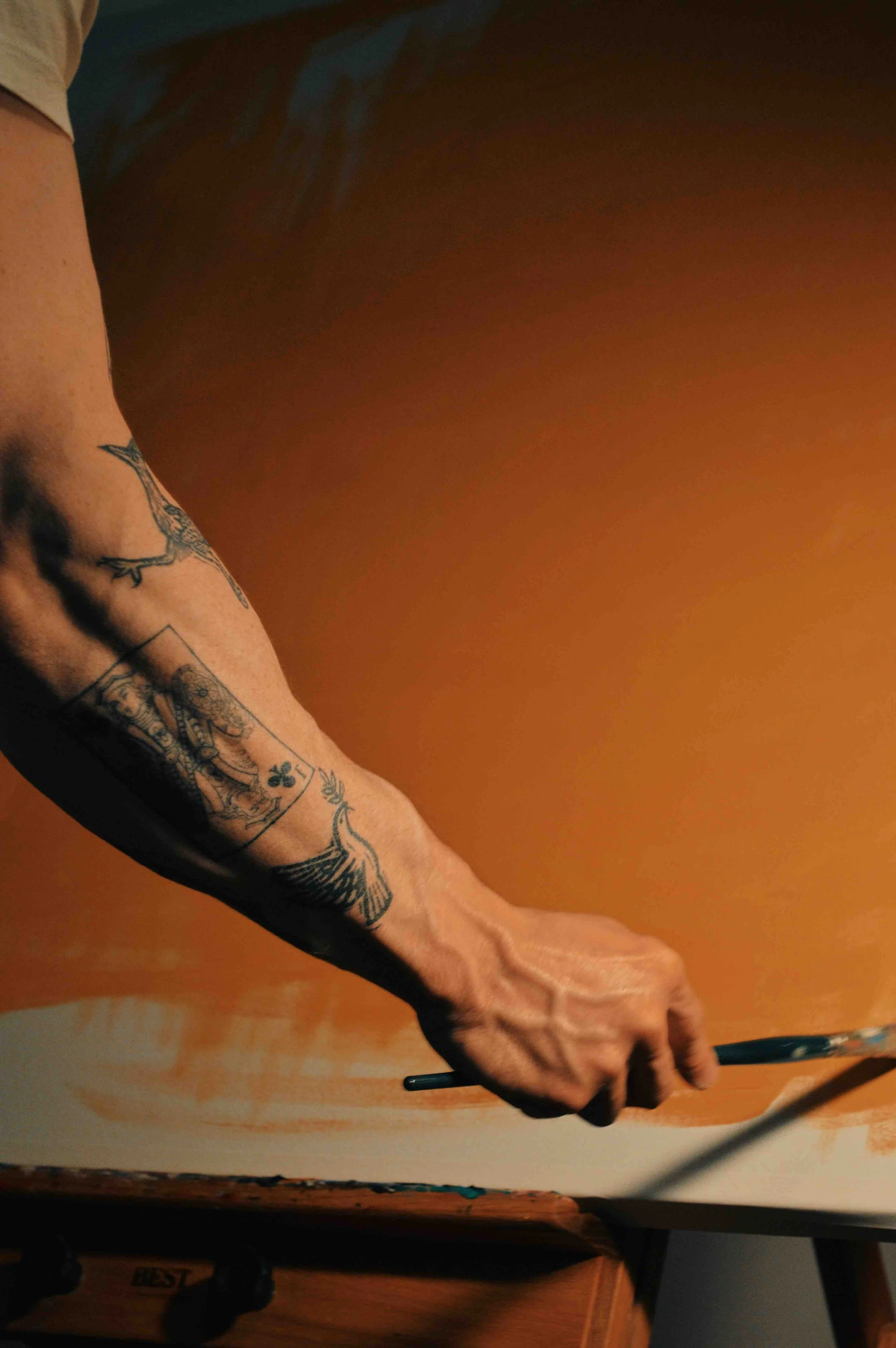 A photo of a tattooed forearm flexing while holding a paintbrush before a painting.