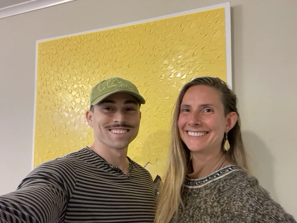 Kevin Koza and a patron smiling before a yellow painting.