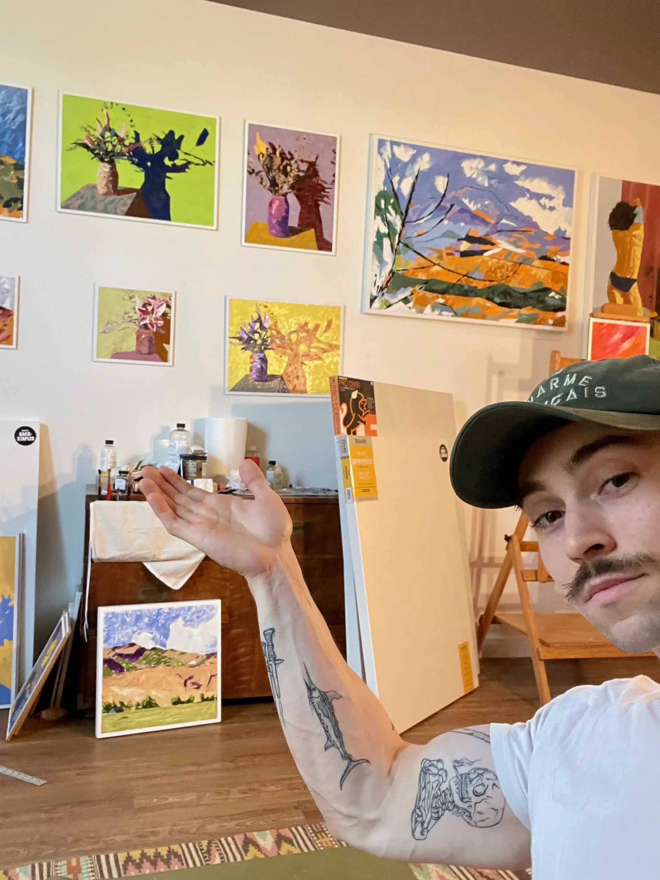 Kevin Koza waving to the selection of paintings available on his wall.