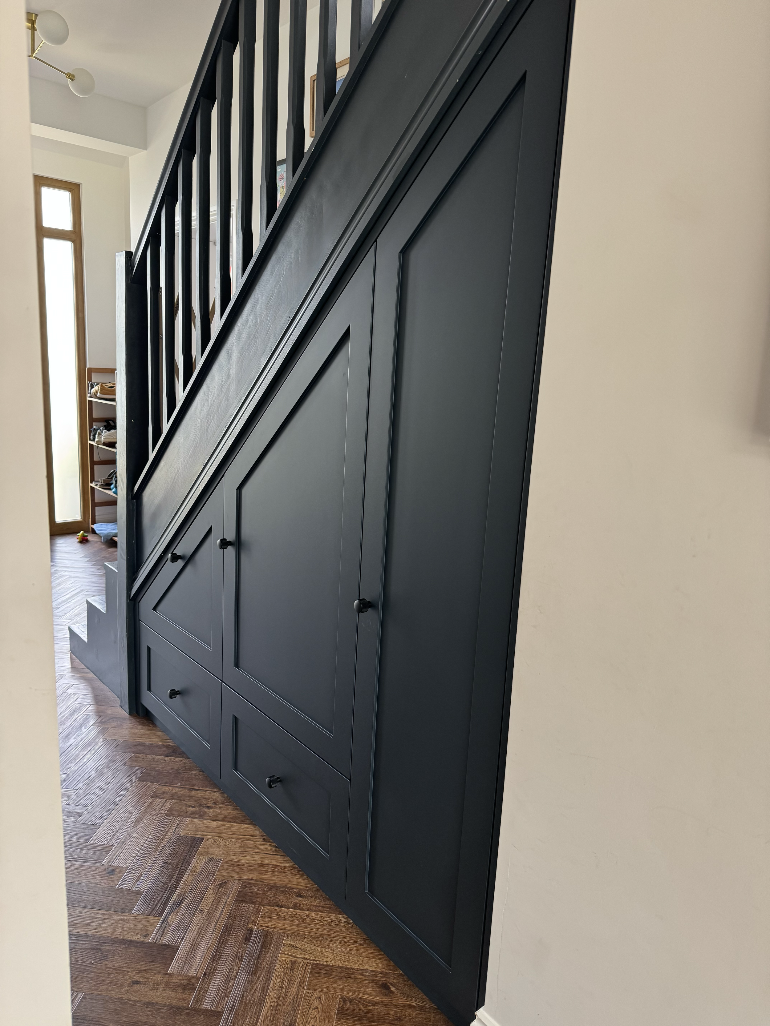 Dark blue built-in storage cabinet under staircase in a house with wooden flooring.