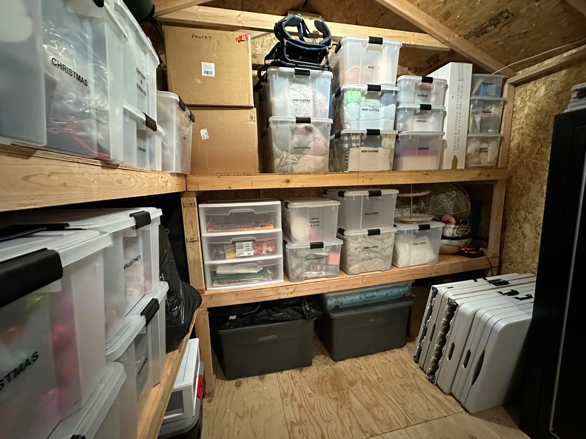 Wooden shelves in a garage or storage room holding a pile of storage bins and boxes. Styled by Tidy Doon, Los Angeles.