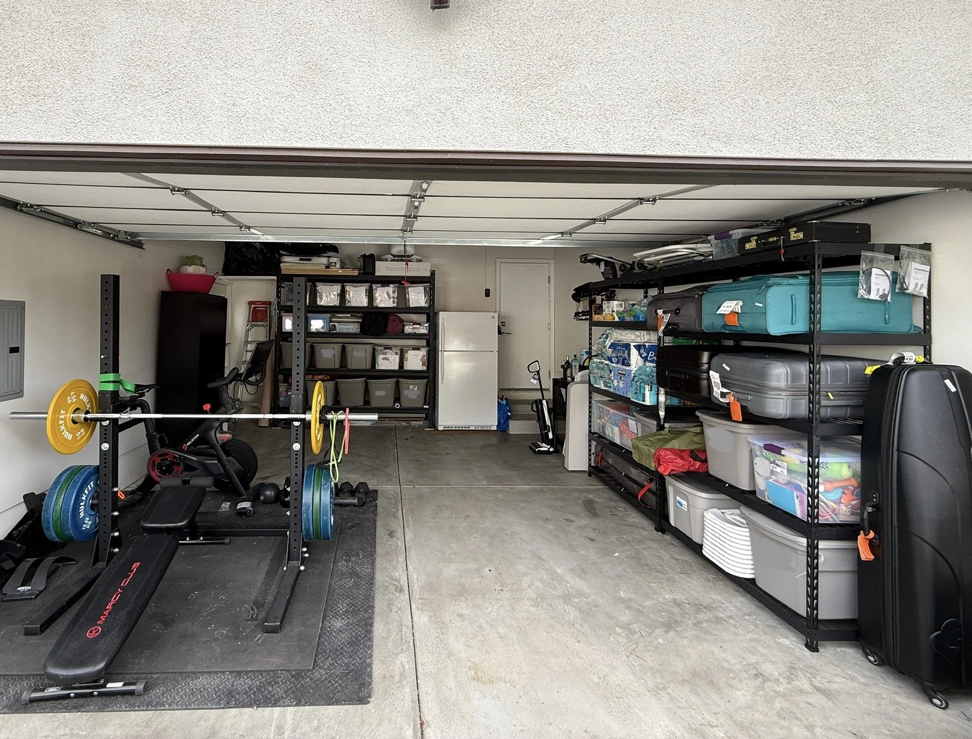Organized garage with gym equipment on the left and metal shelving with labeled storage bins on the right. Styled by Tidy Doon, Los Angeles.