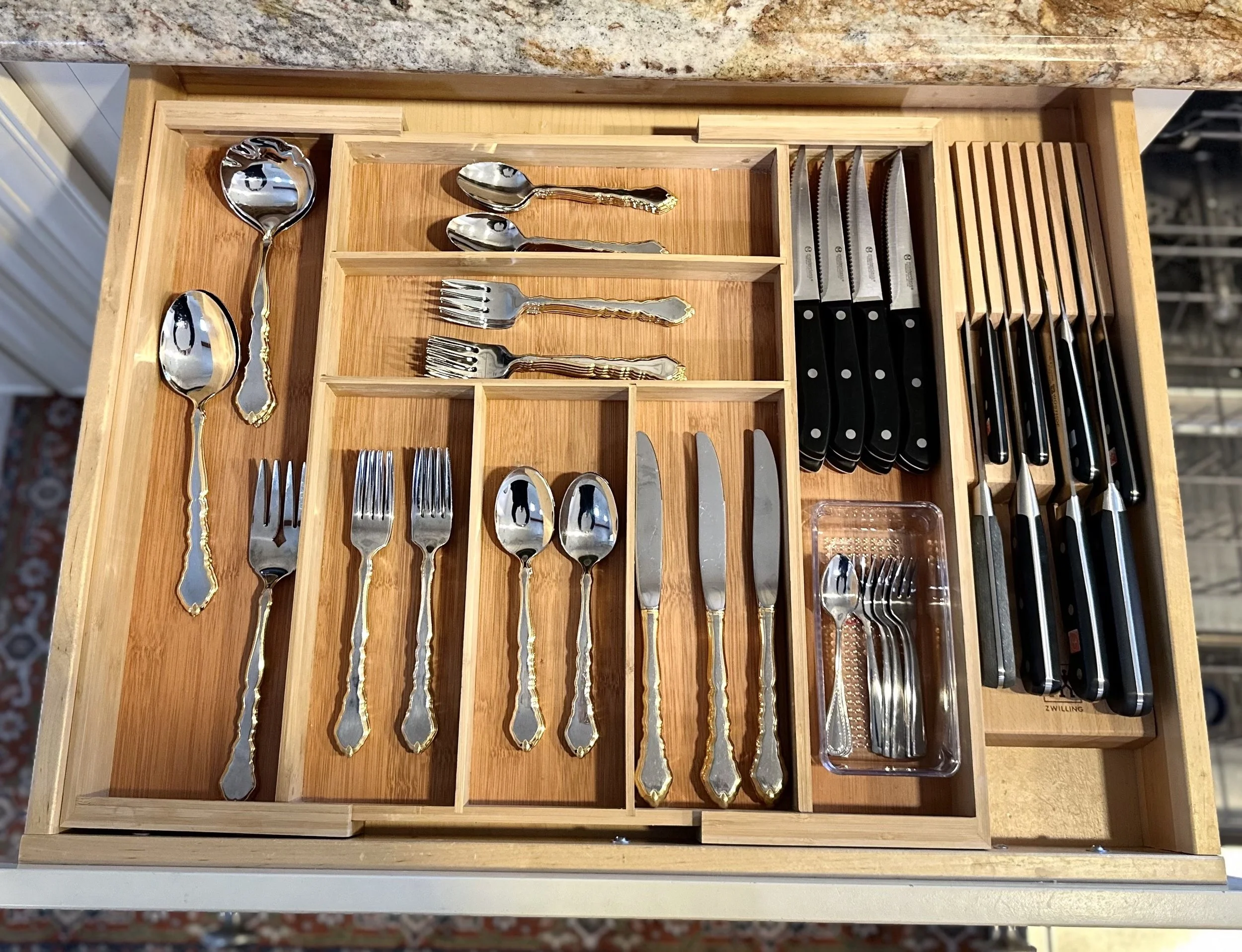 Organized wooden cutlery drawer with silverware and knives arranged in separate compartments. Includes forks, spoons, and butter knives. Styled by Tidy Doon, Los Angeles.