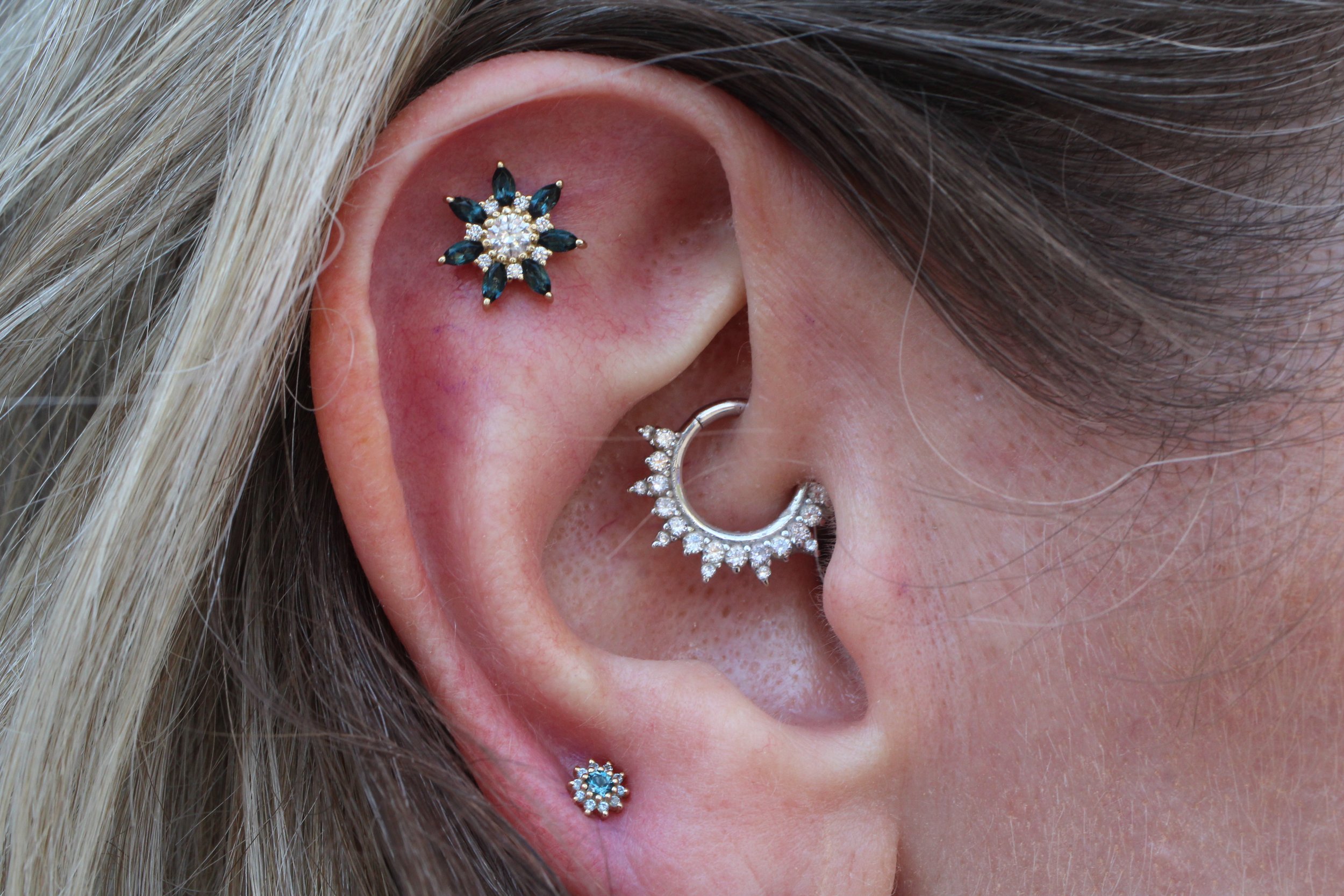 Close-up of an ear with a Daith piercing and a flat piercing with genuine diamond and blue stone jewelry 