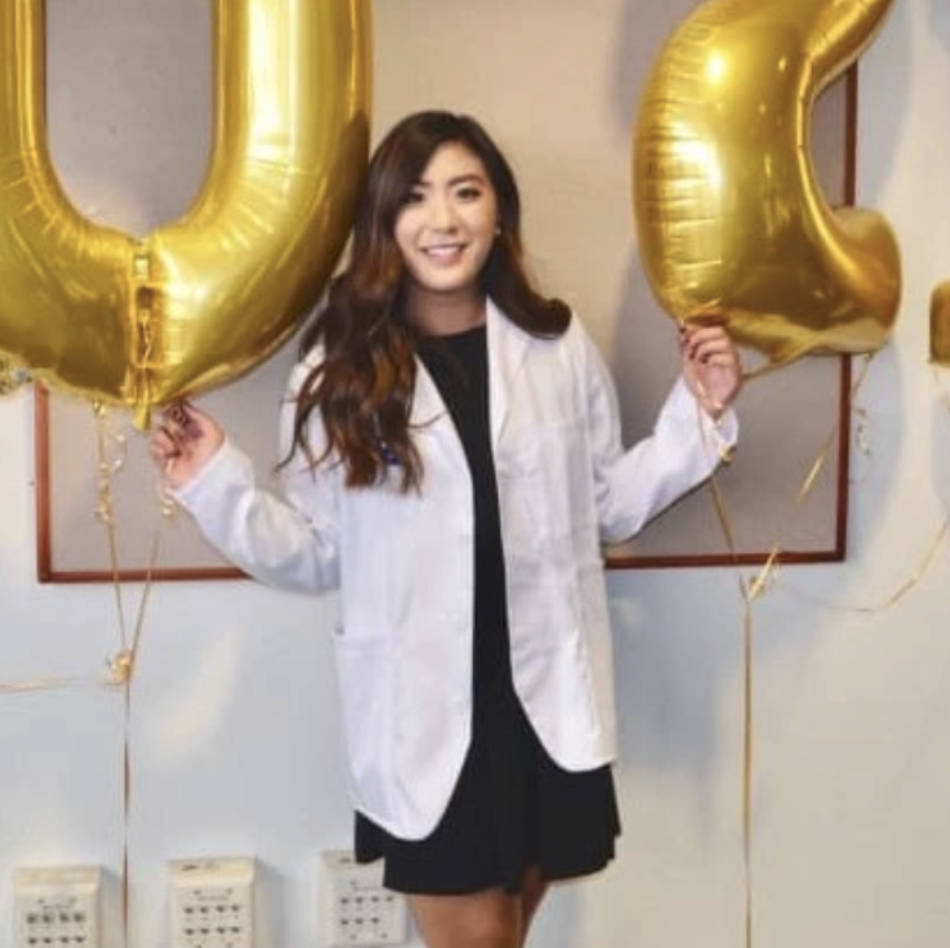A young woman with long, wavy hair is holding two large gold balloons that form the numbers 0 and 2, celebrating a special occasion.