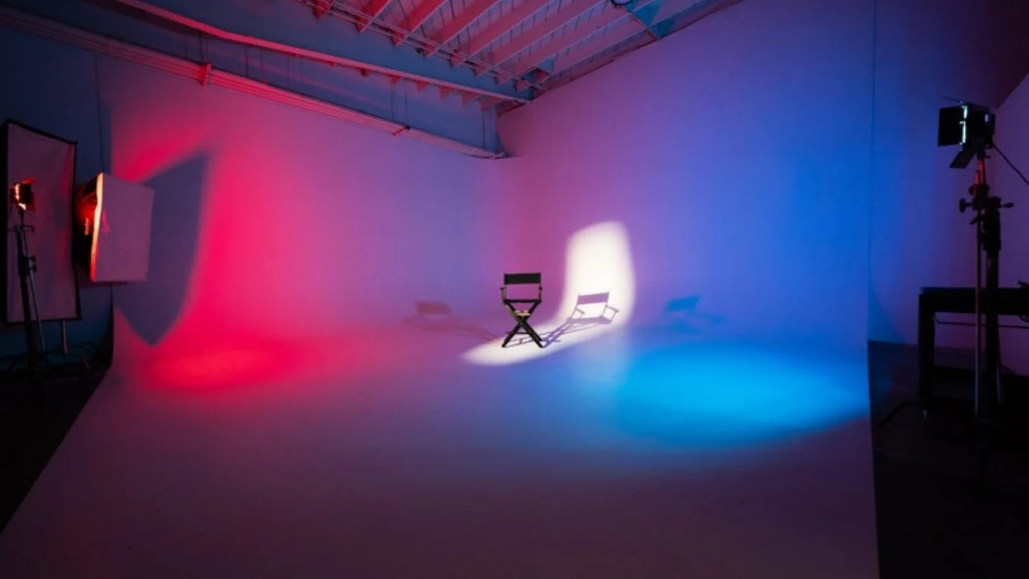 A cyclorama studio lit in red, violet and blue with a director's chair at centre