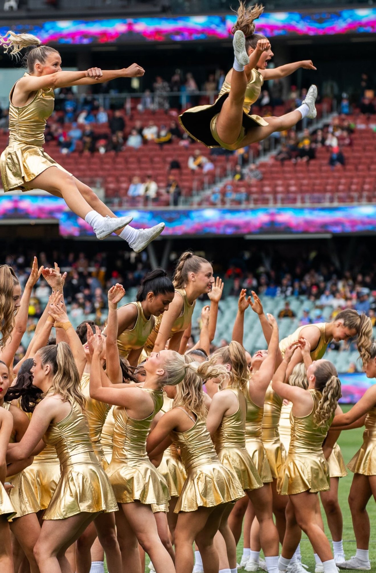 Dancers in gold launching a flyer above the field in front of a packed stadium