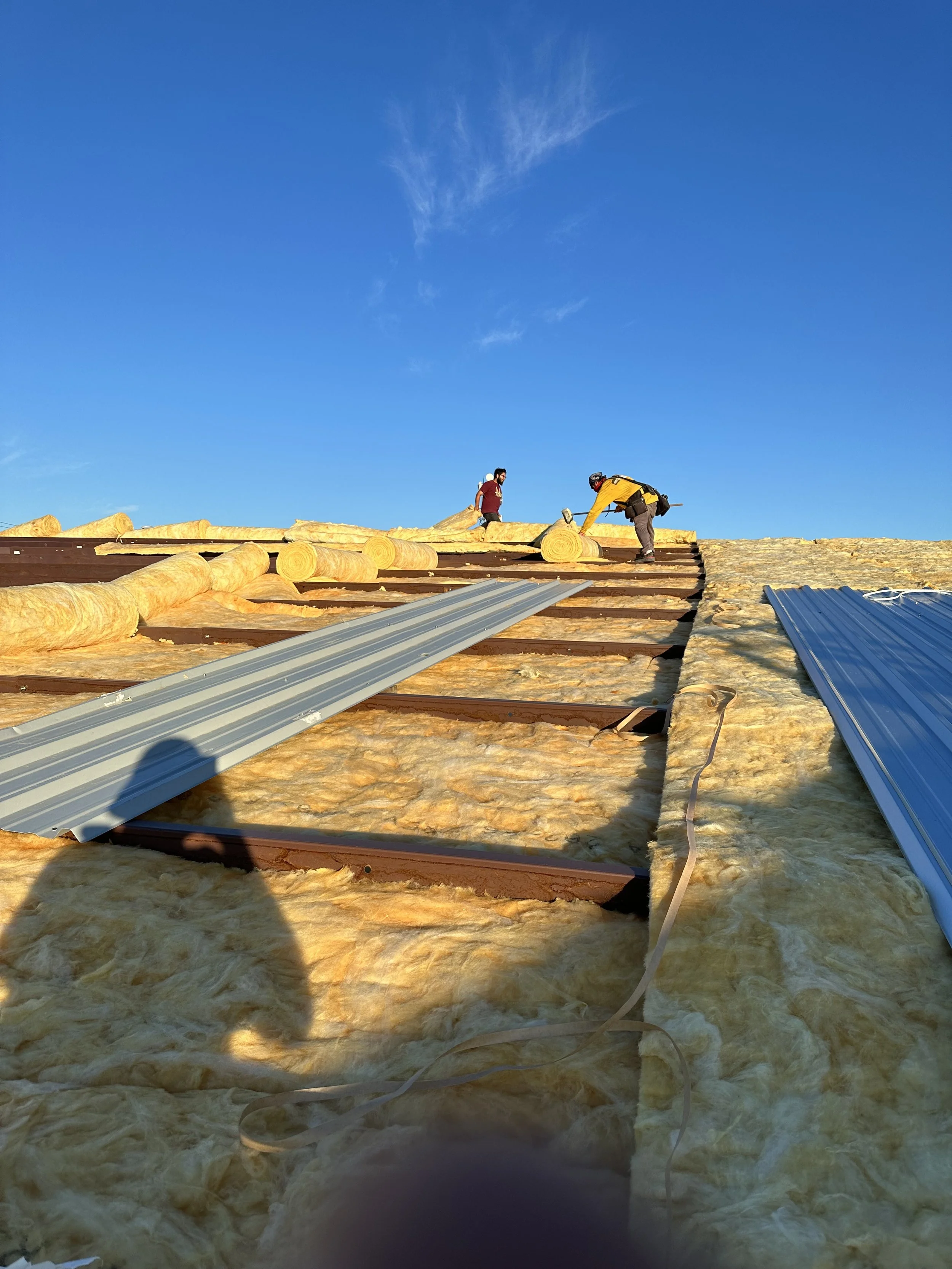 Roof work to a steel metal frame building with 2 workers on top of insulation used for a growing facility