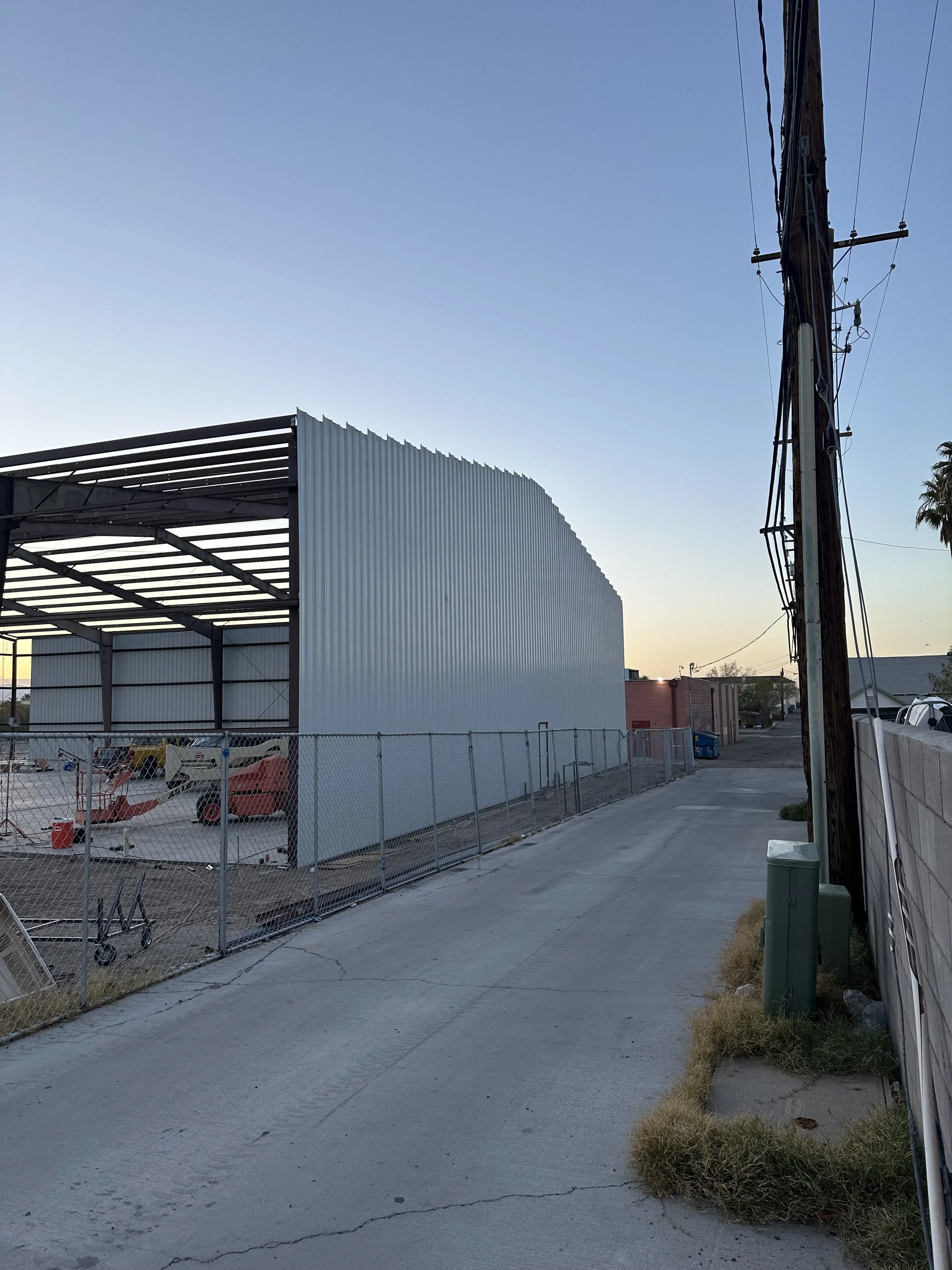 Back alley view of a metal framing to a steel building. Wire fencing around the lot with a concrete slab base
