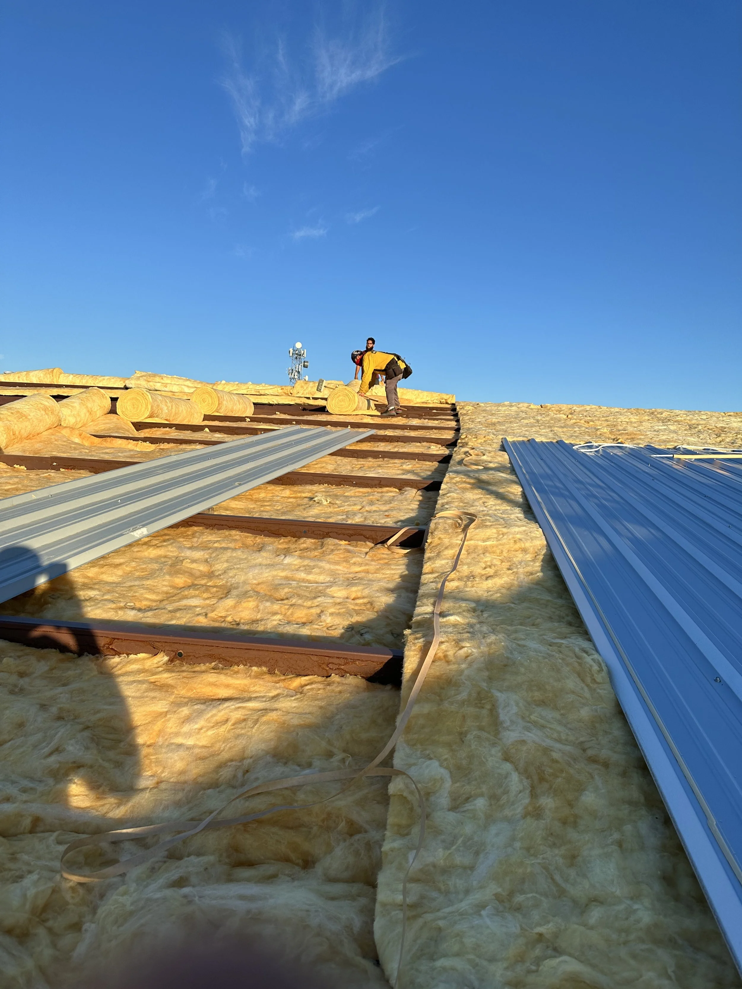 Roof work to a steel metal frame building with 2 workers on top of insulation used for a growing facility