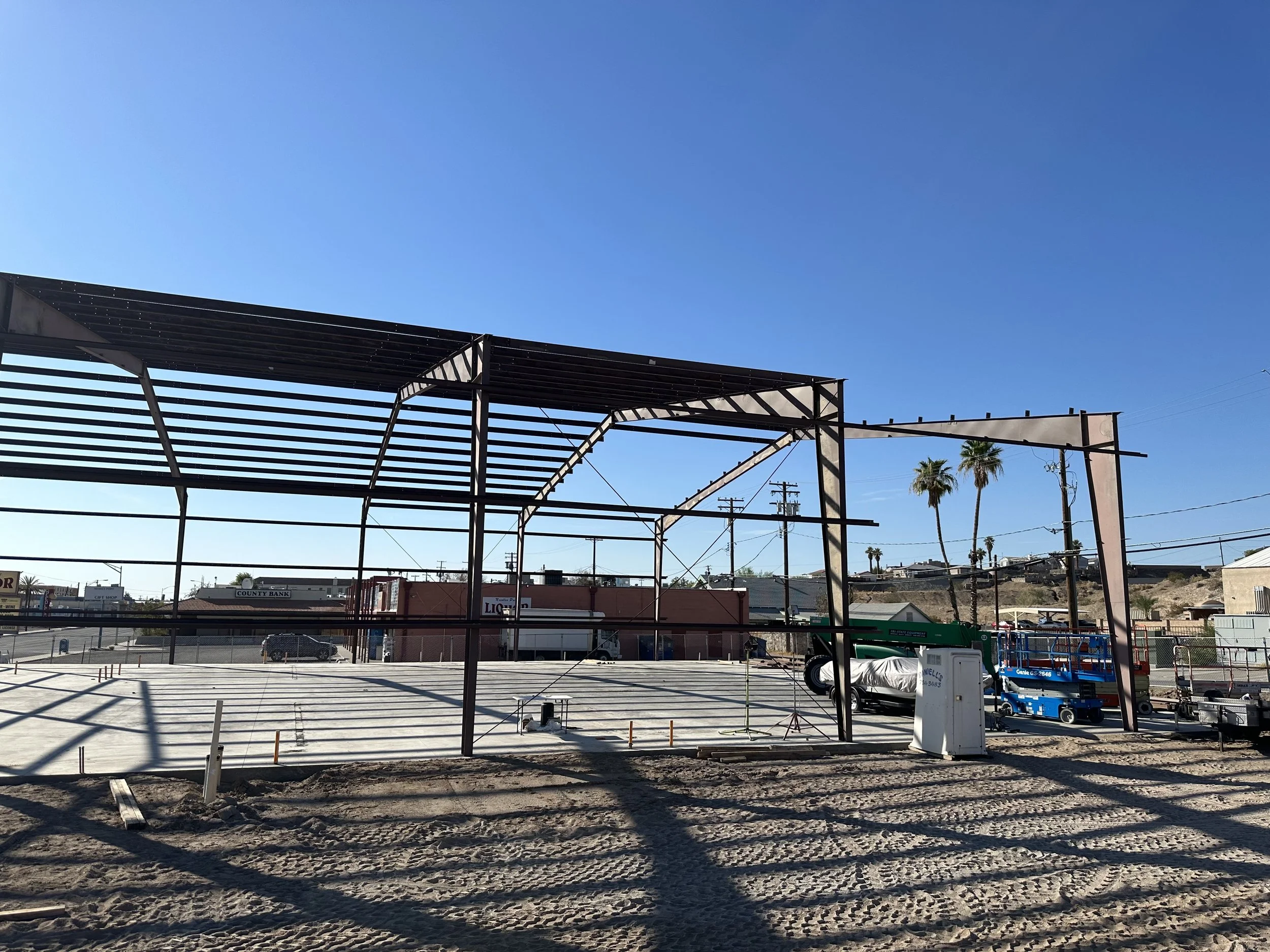 Side view of a metal framing to a steel building. Wire fencing around the lot with a concrete slab base