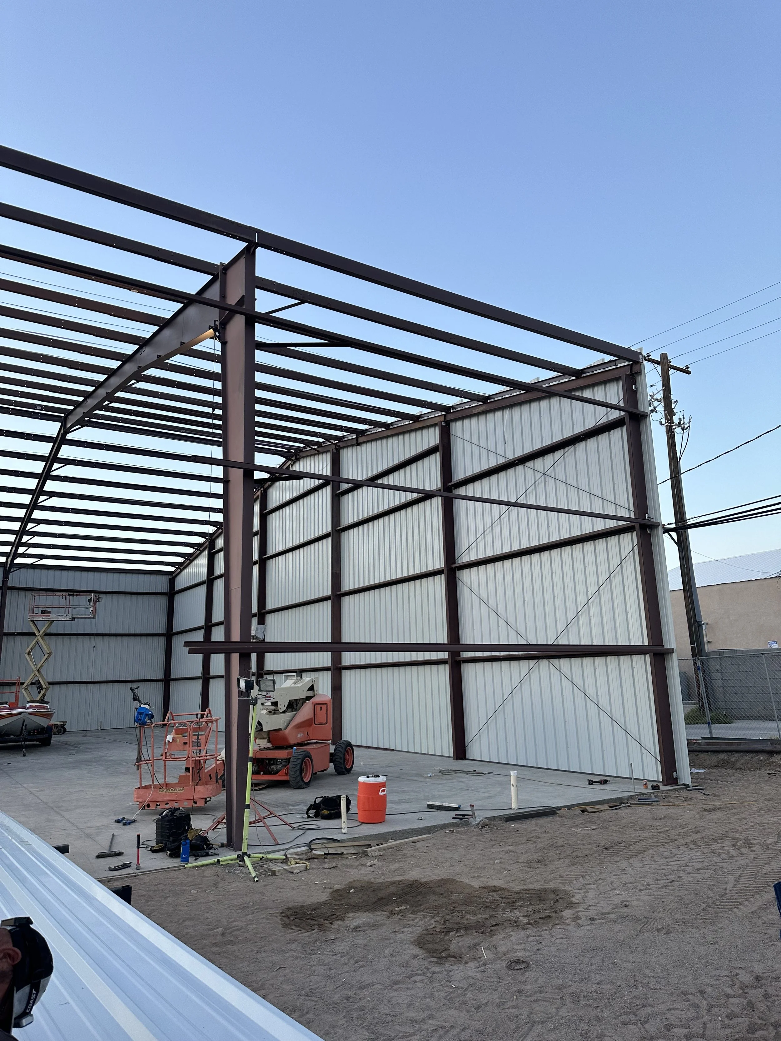 Side view of a steel building with some siding added to the walls. scissor lift and other equipment awaiting use