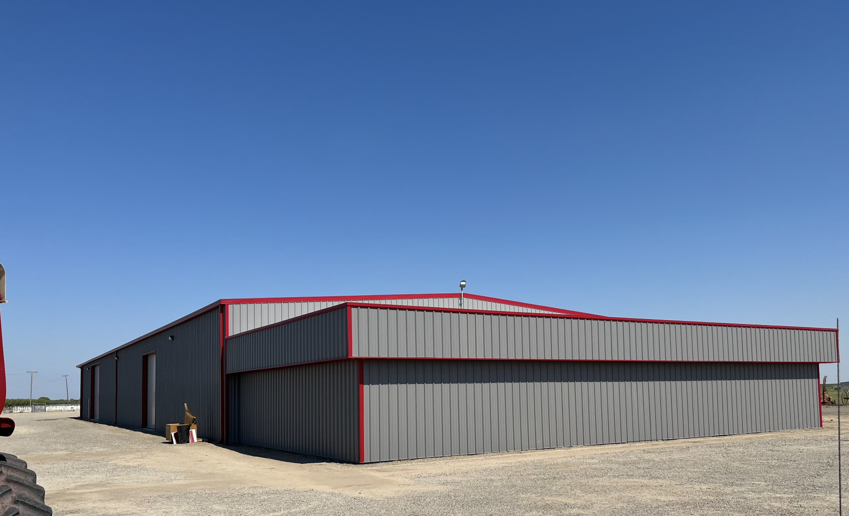 Outside back view of steel building erected for tractor storage and display located in Southern California. Grey paint with a red trim around the building. 